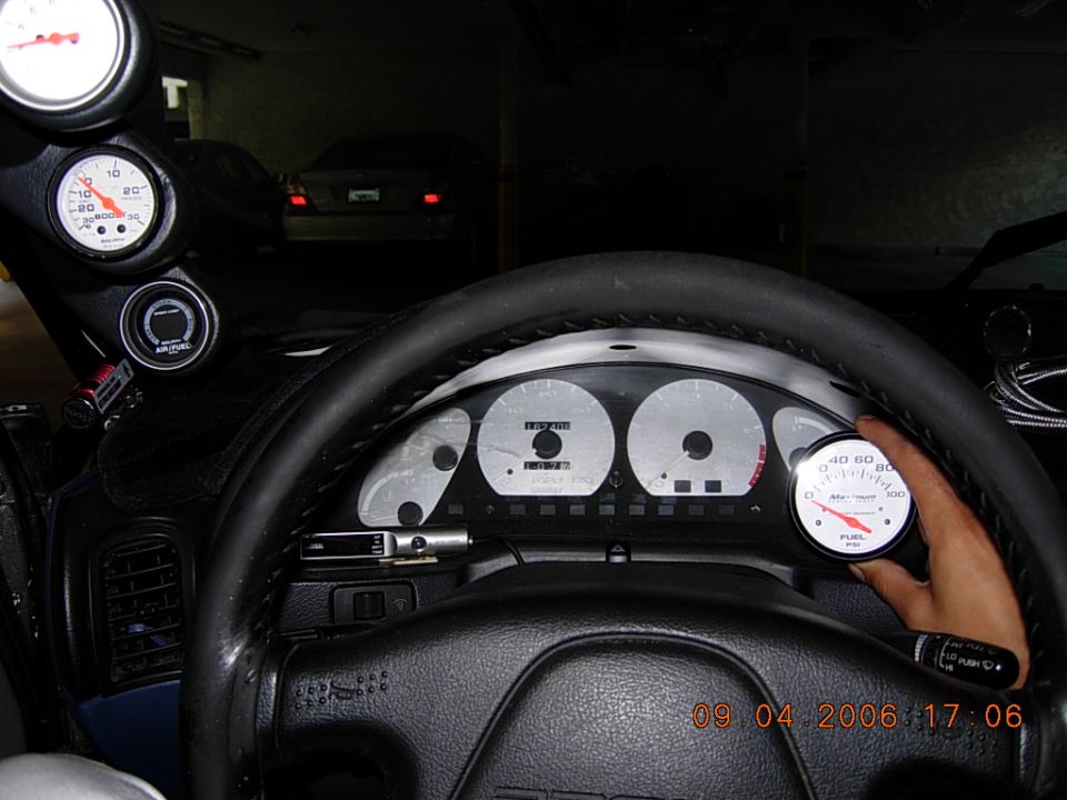 Hand holding a fuel pressure gauge at the instrument cluster, A-pillar gauge pod at left