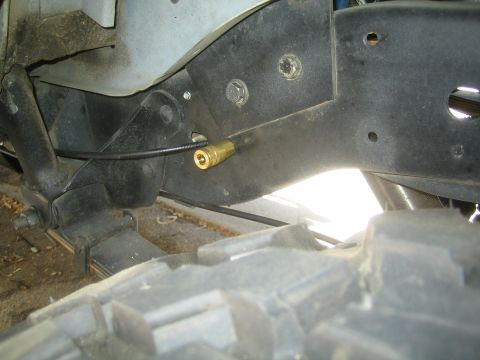 1990 Ford Bronco - brass fitting on an air line routed through a black plastic fender liner above a chunky off-road tire.