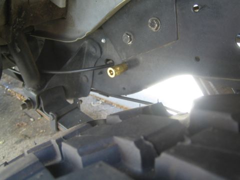 1990 Ford Bronco - brass air-line fitting under a vehicle's black fender liner, with a knobby off-road tire visible below.
