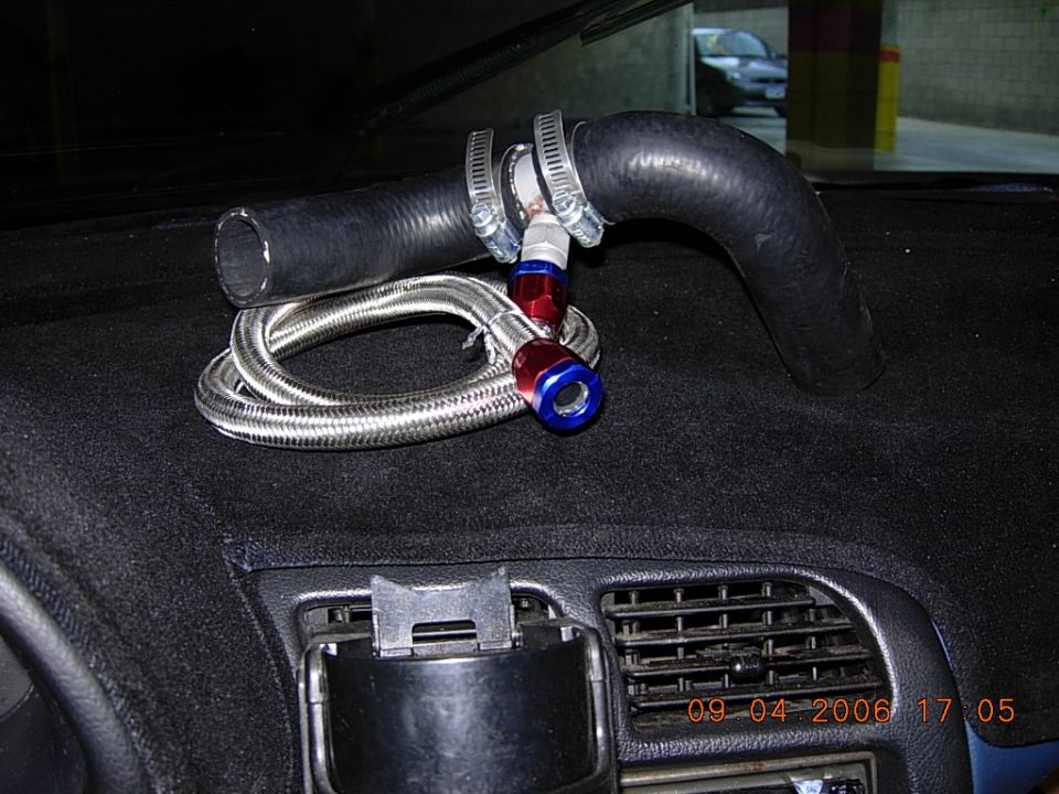 Braided steel line with red/blue AN fittings and black radiator hose on a car dashboard