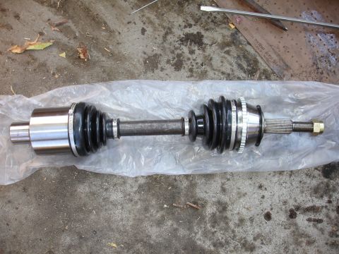 1993 Ford Taurus - A CV axle assembly, likely for a front-wheel-drive vehicle, is presented on a plastic sheet against a concrete background.