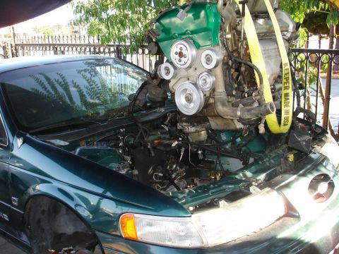 1993 Ford Taurus - Engine removal in progress on a green 1993 Ford Taurus. The vehicle appears to be undergoing maintenance or an upgrade.