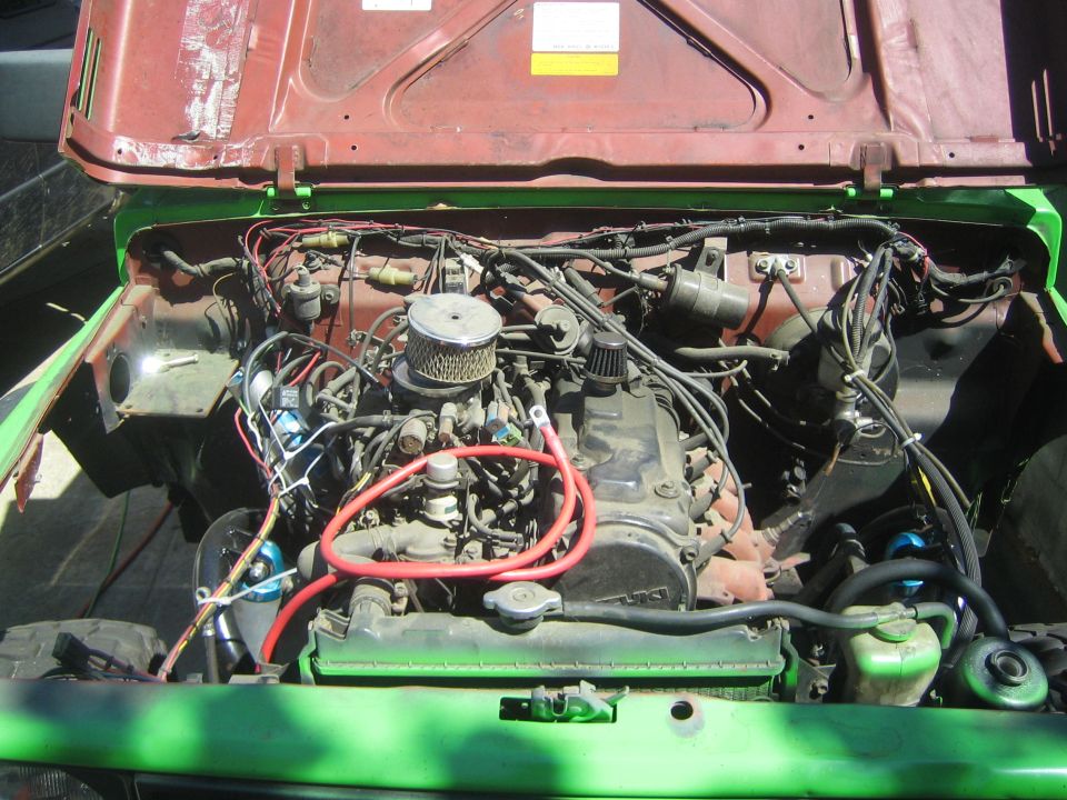 engine bay of a green vehicle with the hood open, showing the engine and wiring