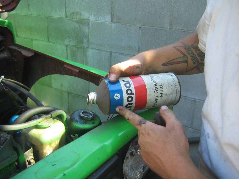 Person pouring Mopar power steering fluid into green vehicle engine bay