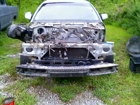 2002 Ford Crown Victoria - The front of a white 2002 Ford Crown Victoria is heavily damaged and disassembled, with its engine and wiring exposed.