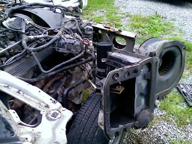Disassembled car engine, radiator support, and HVAC blower motor housing. Wires and hoses are disconnected