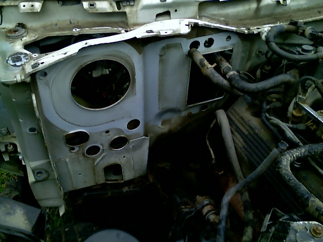 Firewall and engine bay of a disassembled vehicle, showing hoses and metal components