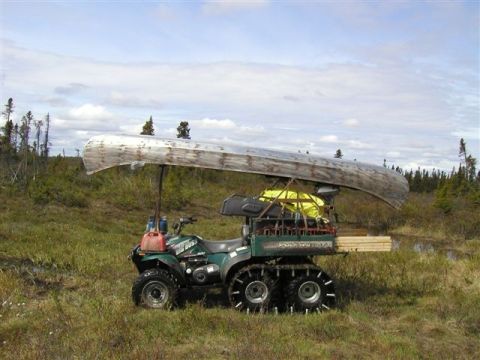 1976 Ford F-150 - An all-terrain vehicle is equipped with tracks and a rack system to transport a canoe and lumber through a marshy landscape.