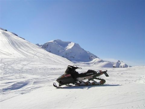 1976 Ford F-150 - A snowmobile rests on a snow-covered mountainside under a clear blue sky.