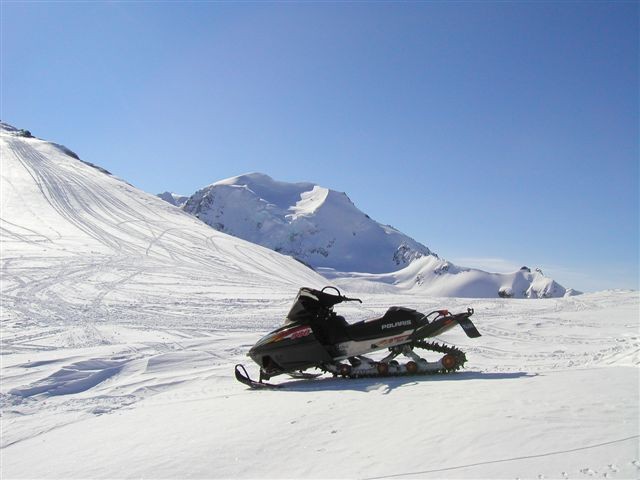 Black and white snowmobile parked on a snowy slope with mountains in the background