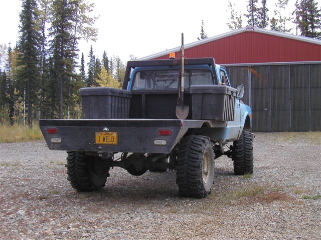 Blue flatbed truck with large tires and a shovel in the bed