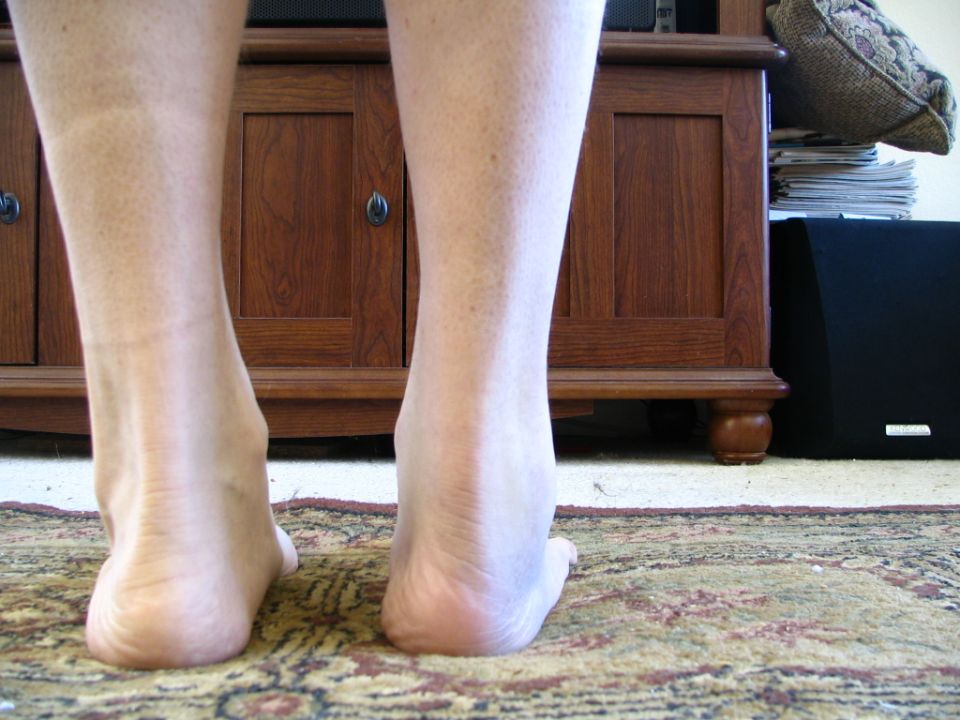 Bare human legs and feet standing on a patterned rug in front of a wooden cabinet