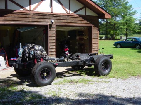 1991 Ford Bronco - A vehicle chassis with its engine and wheels is parked outside a garage, with another car in the background.