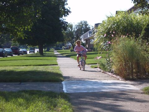 1993 Ford Bronco - A young girl rides her bicycle down a sidewalk in a residential neighborhood on a sunny day.