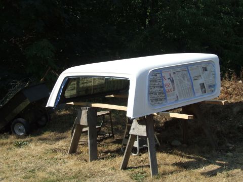 1979 Ford Bronco - A white truck bed cap is propped up on sawhorses outdoors, with newspaper taped over the windows.
