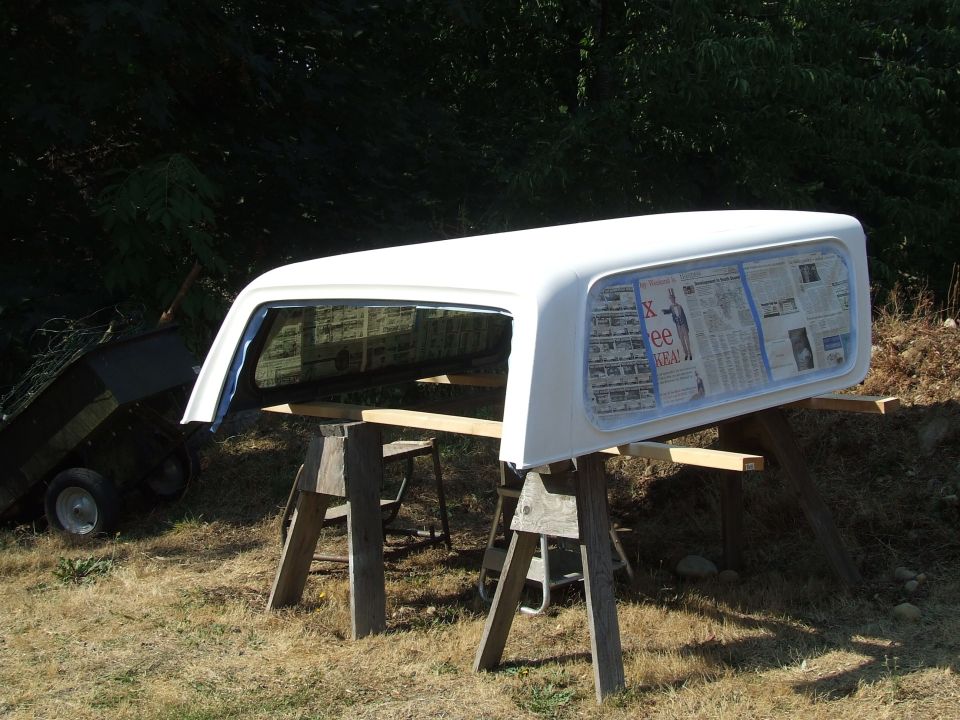 white truck bed cap on sawhorses, newspaper taped to windows