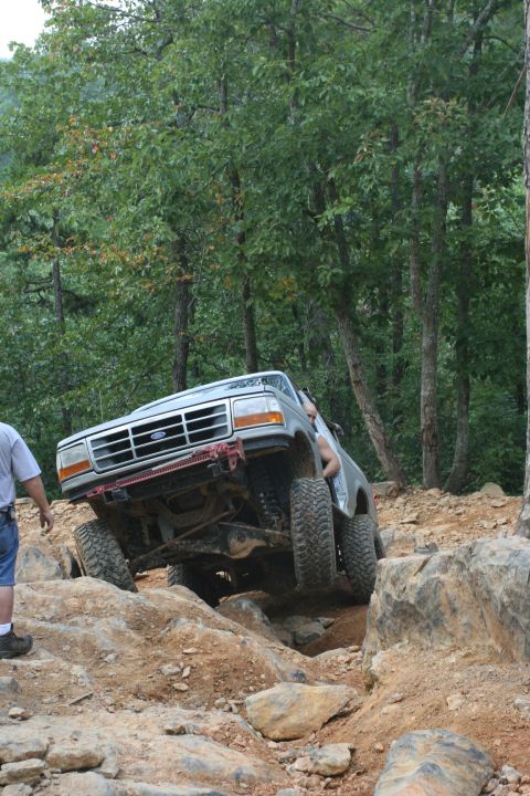 1990 Ford Bronco - A Ford Bronco navigates a rocky off-road course with trees in the background.
