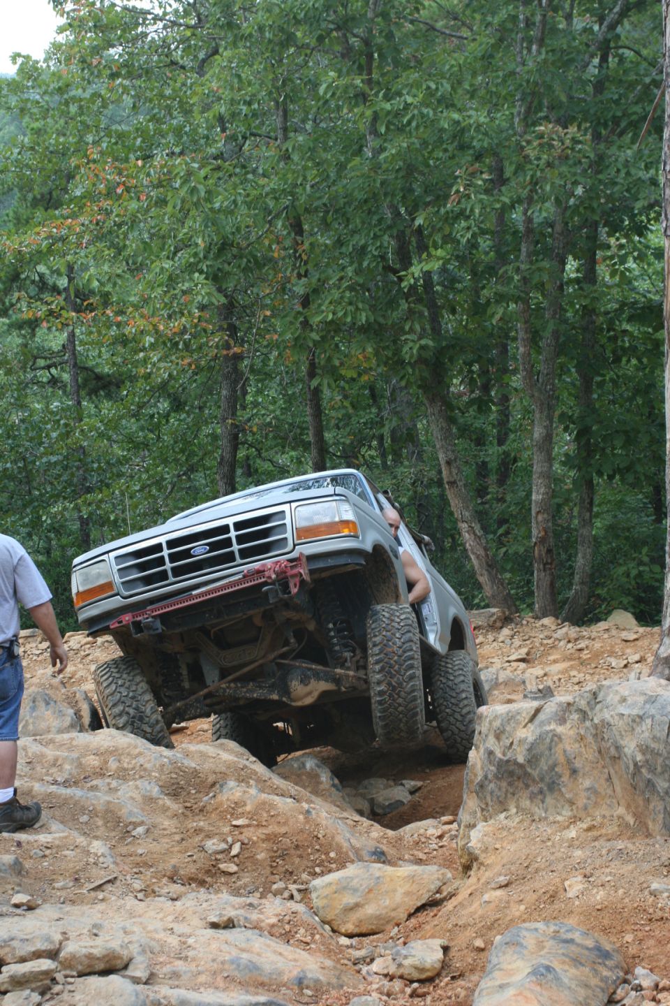 Ford Bronco climbing over rocks on a trail. Driver's side is lifted high