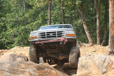 1990 Ford Bronco - A silver Ford Bronco tackles a challenging rocky trail, demonstrating its off-road capabilities.