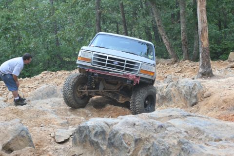 1990 Ford Bronco - A man observes a modified Ford Bronco navigating a challenging rocky terrain.