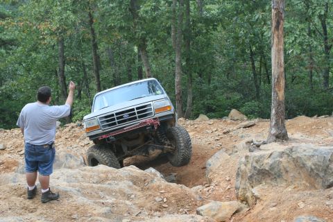 1990 Ford Bronco - A man watches a silver Ford Bronco navigate a rocky off-road course.