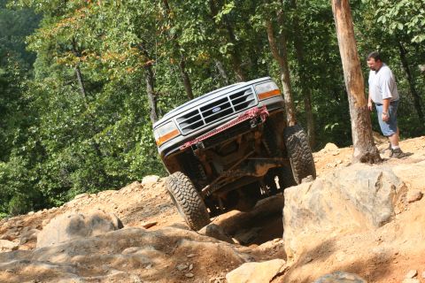 1990 Ford Bronco - A white Ford Bronco navigates a challenging rocky incline, with a man watching from the side.