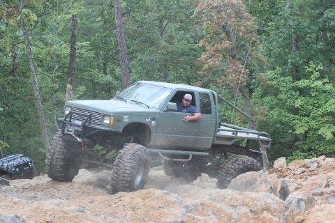1990 Ford Bronco - A modified green pickup truck tackles a challenging off-road course with large tires and a lifted suspension.