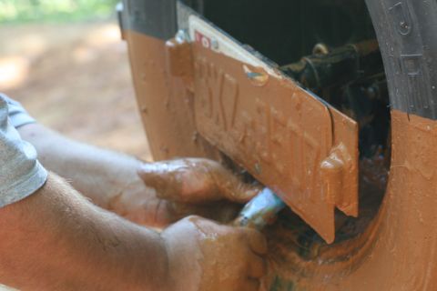 1990 Ford Bronco - Hands clean mud from a license plate on a heavily soiled vehicle.