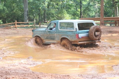 1990 Ford Bronco - Ford Bronco navigates a muddy trail, kicking up water and dirt.