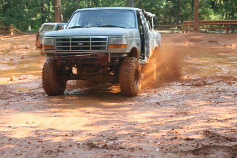 1990 Ford Bronco - This Ford Bronco is navigating a muddy off-road course, with another vehicle in the background.