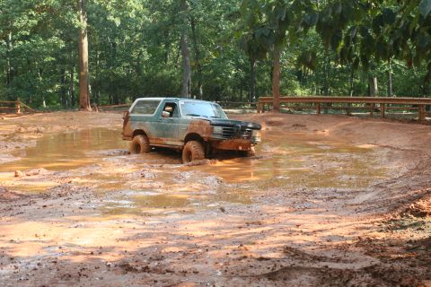 1990 Ford Bronco - A green Ford Bronco navigates a muddy obstacle course, its front end partially submerged.