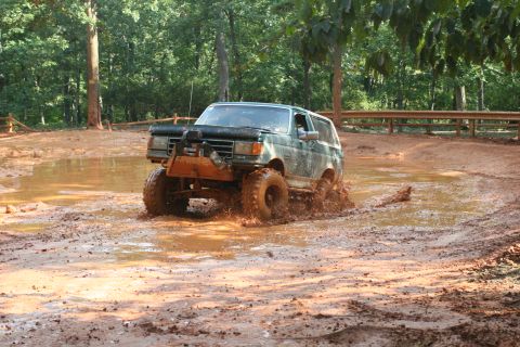 1990 Ford Bronco - This 1990 Ford Bronco is navigating a muddy off-road course, splashing water and mud.