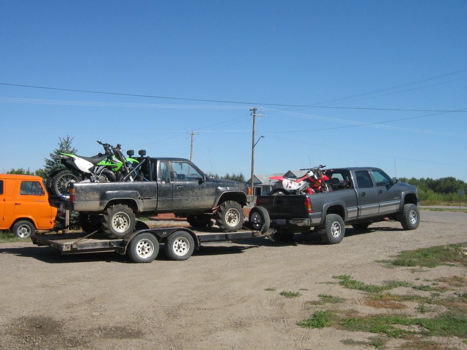 Orange van, black pickup on trailer with dirt bike, and gray pickup with dirt bike parked outside