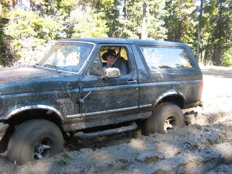 Ford Bronco stuck in mud, driver wearing a hat