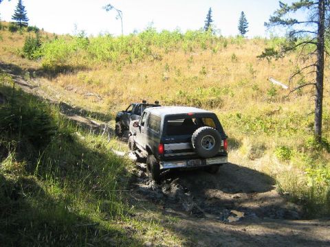 1995 Ford Bronco - Two SUVs navigate a muddy off-road trail on a sunny day.