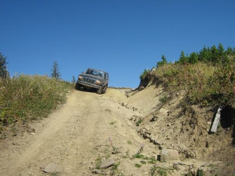 1995 Ford Bronco - Ford Bronco tackling an off-road trail under a clear blue sky.