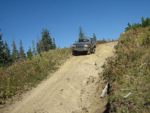 1995 Ford Bronco - A 1995 Ford Bronco navigates a challenging dirt path on a sunny day, surrounded by natural terrain.