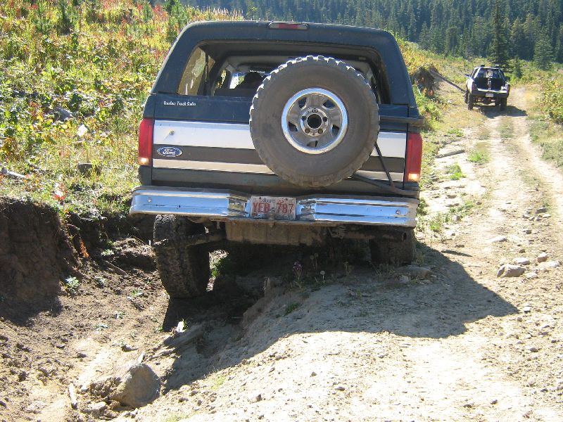 1995 Ford Bronco on a dirt trail, rear view, spare tire mounted. Another vehicle is visible ahead on the trail