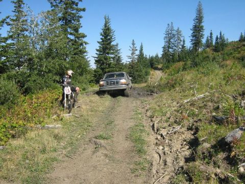 1995 Ford Bronco - A 1995 Ford F-Series truck navigates a muddy trail while a dirt bike rider watches from the side of the path.