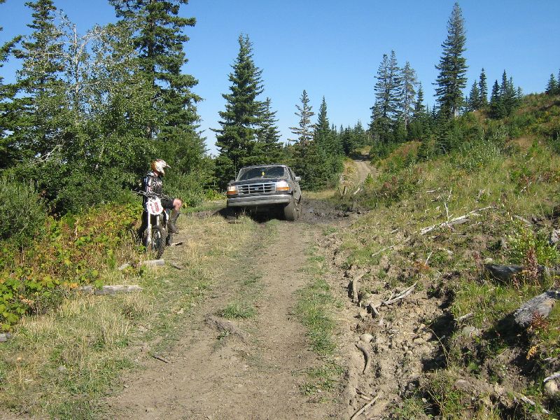 1995 Ford F-Series truck driving through mud on a dirt road, dirt bike rider nearby