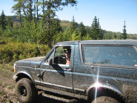 1995 Ford Bronco - A driver navigates a muddy trail in a Ford Bronco, surrounded by trees and hills.