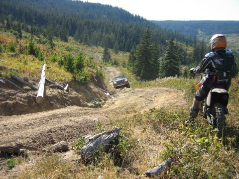 1995 Ford Bronco - A dirt bike rider observes an SUV navigating a challenging off-road trail through a forested landscape.