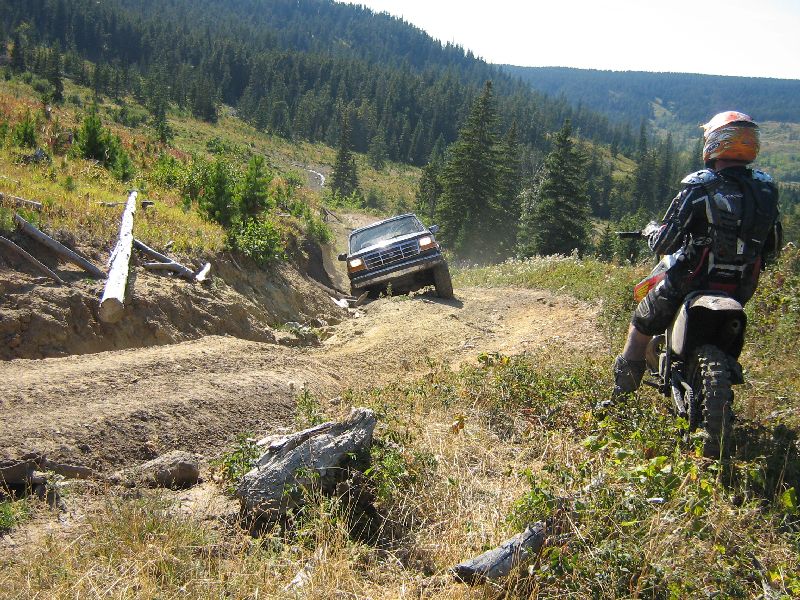 1995 Ford Bronco driving off-road with a dirt bike rider watching