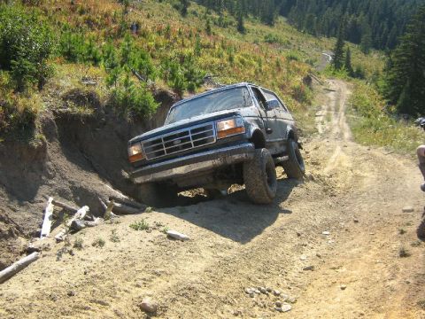 1995 Ford Bronco - A 1995 Ford Bronco tackles a challenging off-road trail on a sunny day.