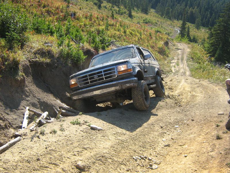 Ford Bronco navigating a steep, dirt trail with trees on the hillside