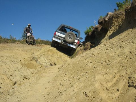 1995 Ford Bronco - A 1995 Ford Bronco navigates a challenging off-road descent, with a dirt bike rider observing nearby.