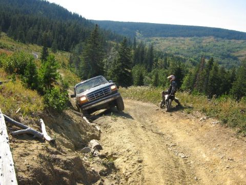 1995 Ford Bronco - A Ford Bronco navigates a challenging off-road trail with a dirt biker observing.