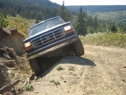 1995 Ford Bronco - Ford Bronco navigating a steep, muddy off-road trail in a wooded area.
