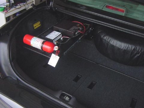 2003 Ford Crown Victoria - The trunk of a vehicle contains a fire extinguisher, a black box with wiring, and a spare tire cover.