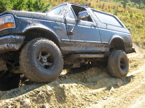 1995 Ford Bronco - This Ford Bronco is covered in mud while navigating a challenging off-road terrain.